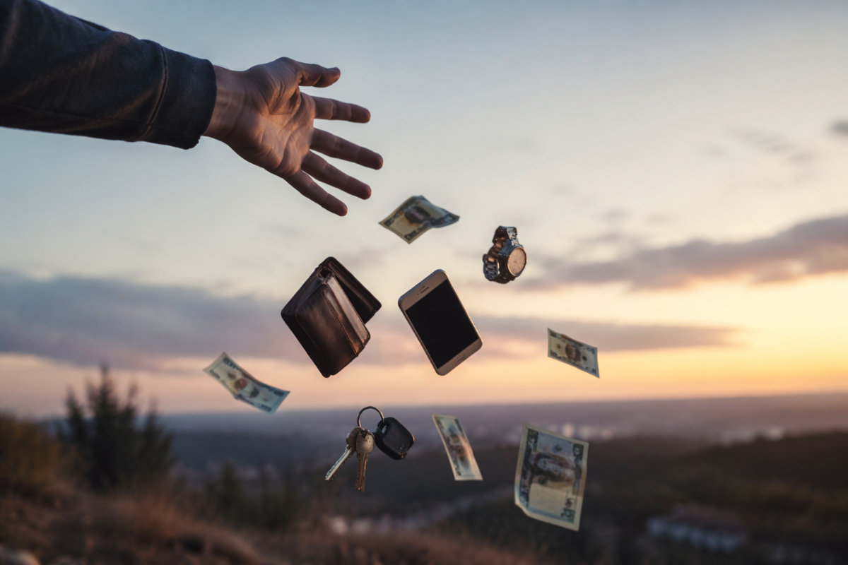Hand lässt Gegenstände wie Geld, Handy und Schlüssel los – Symbol für Verzicht beim Neustart